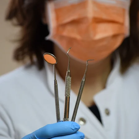 Dental professional holding a mirror and dental instruments.
